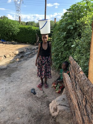 Little Cheri with a very heavy water bucket on her head, preparing to head home.